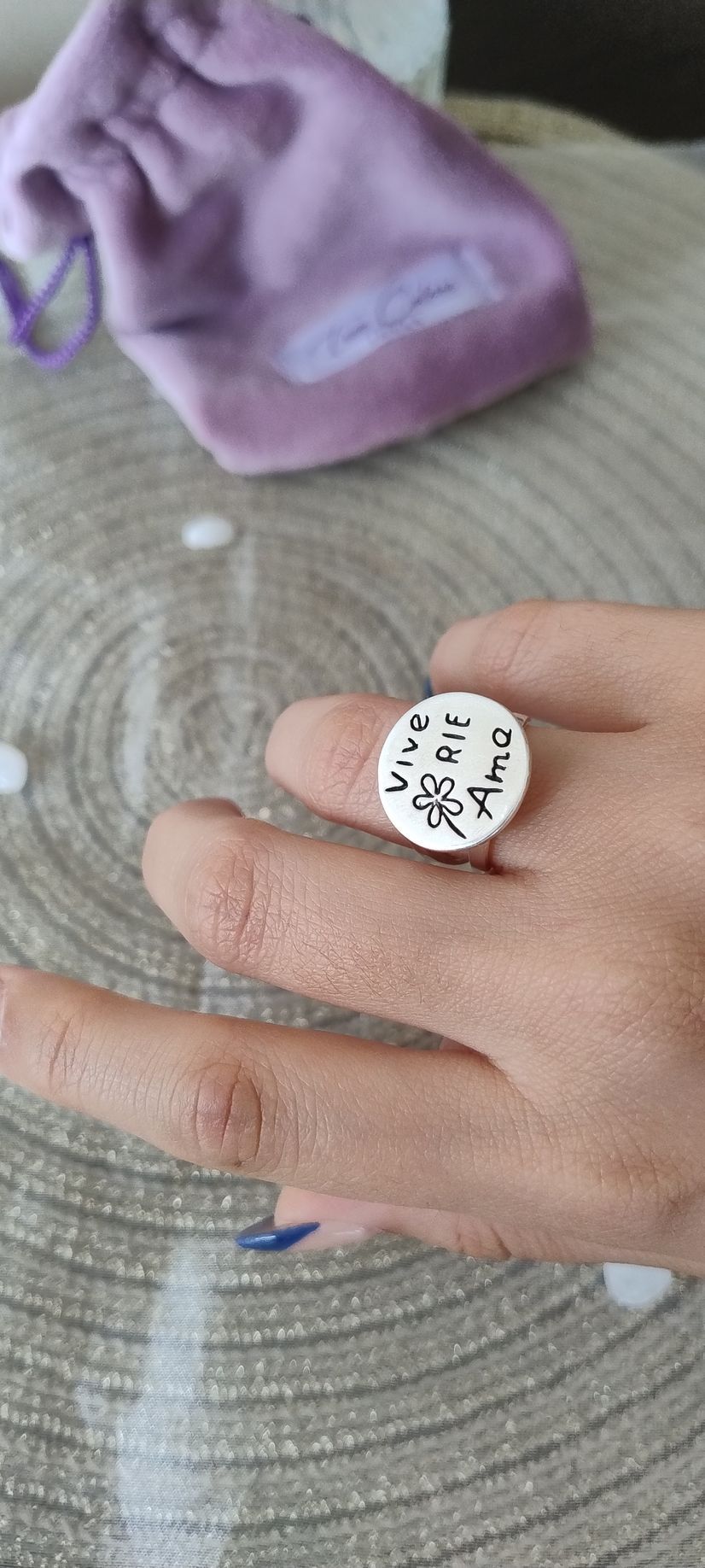 Una mano que lleva un anillo redondo blanco con texto negro, descansa sobre una superficie tejida gris
