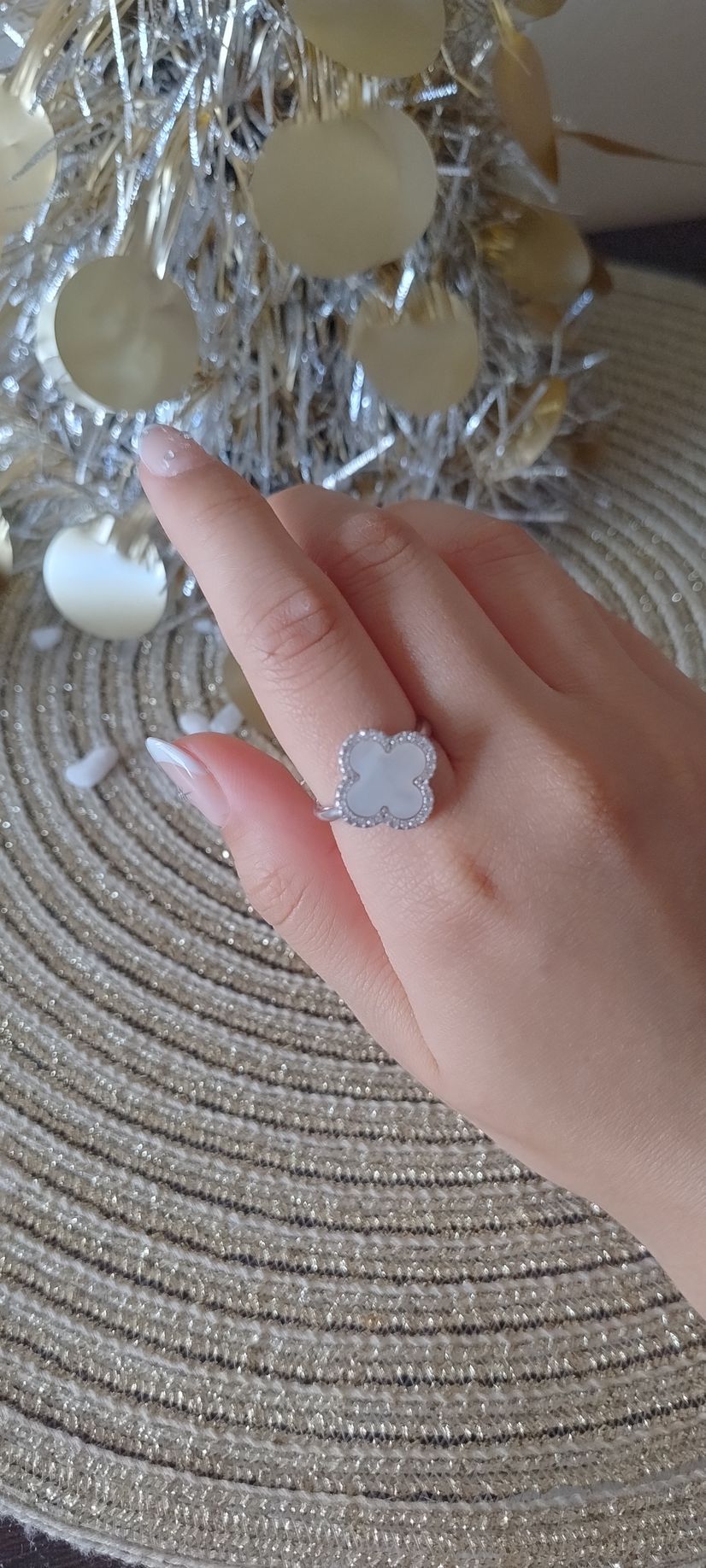 Una mano con un anillo de plata cerca de un portavelas de cristal sobre un mantel individual tejido.