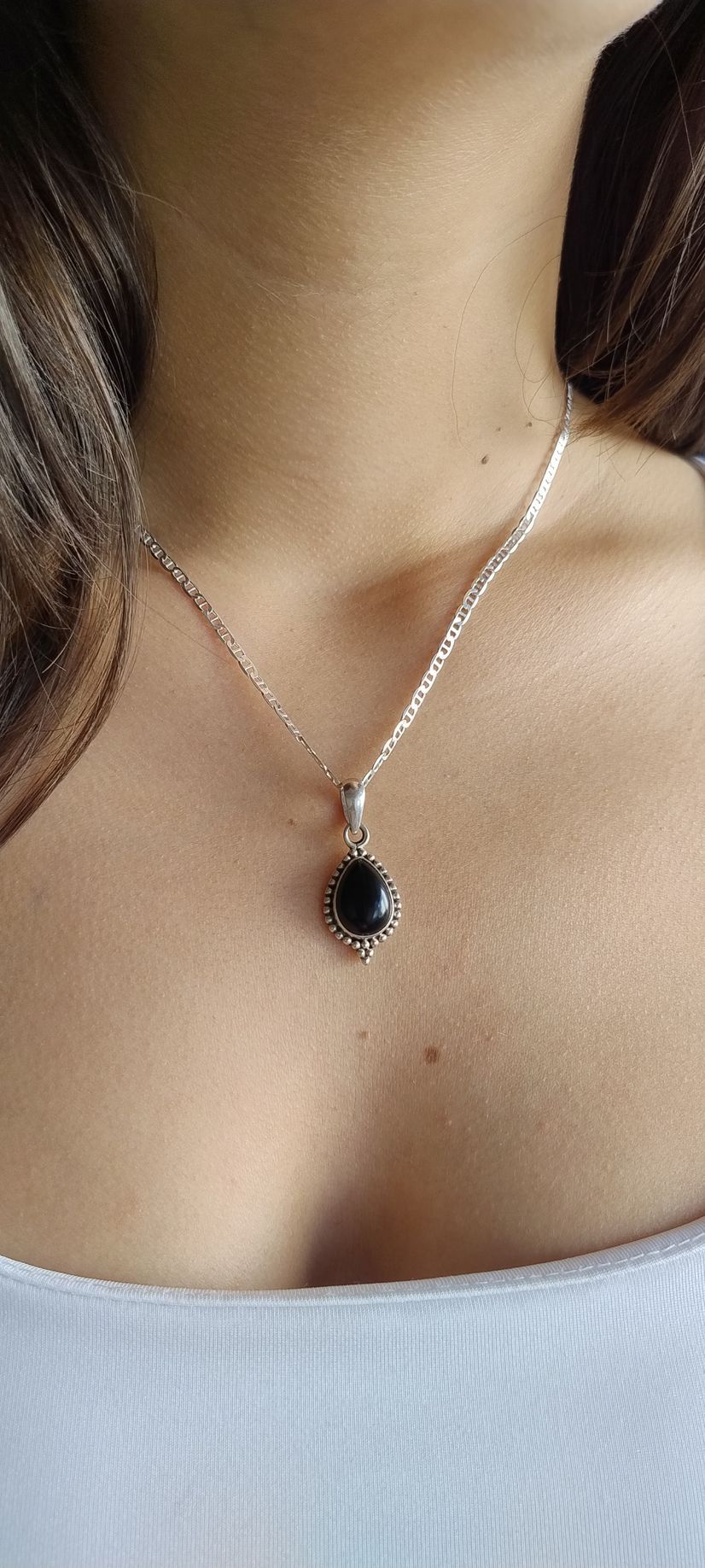 Primer plano de un collar de plata con un colgante oscuro sobre una base blanca.