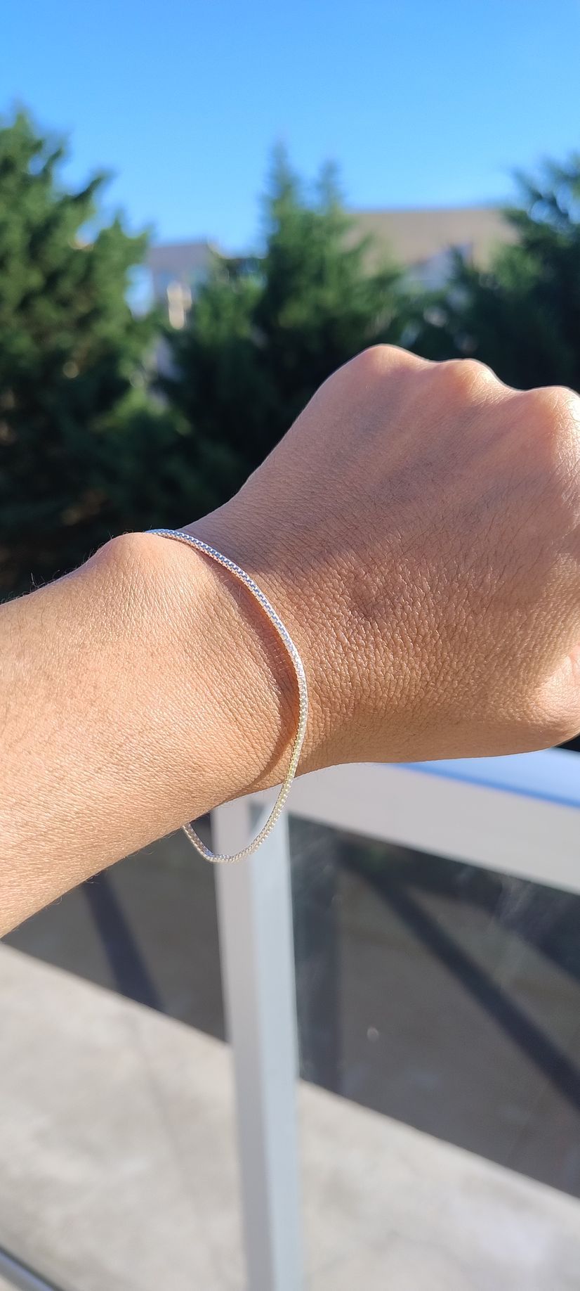 Muñeca iluminada por el sol con una pulsera de plata apoyada en una barandilla blanca al aire