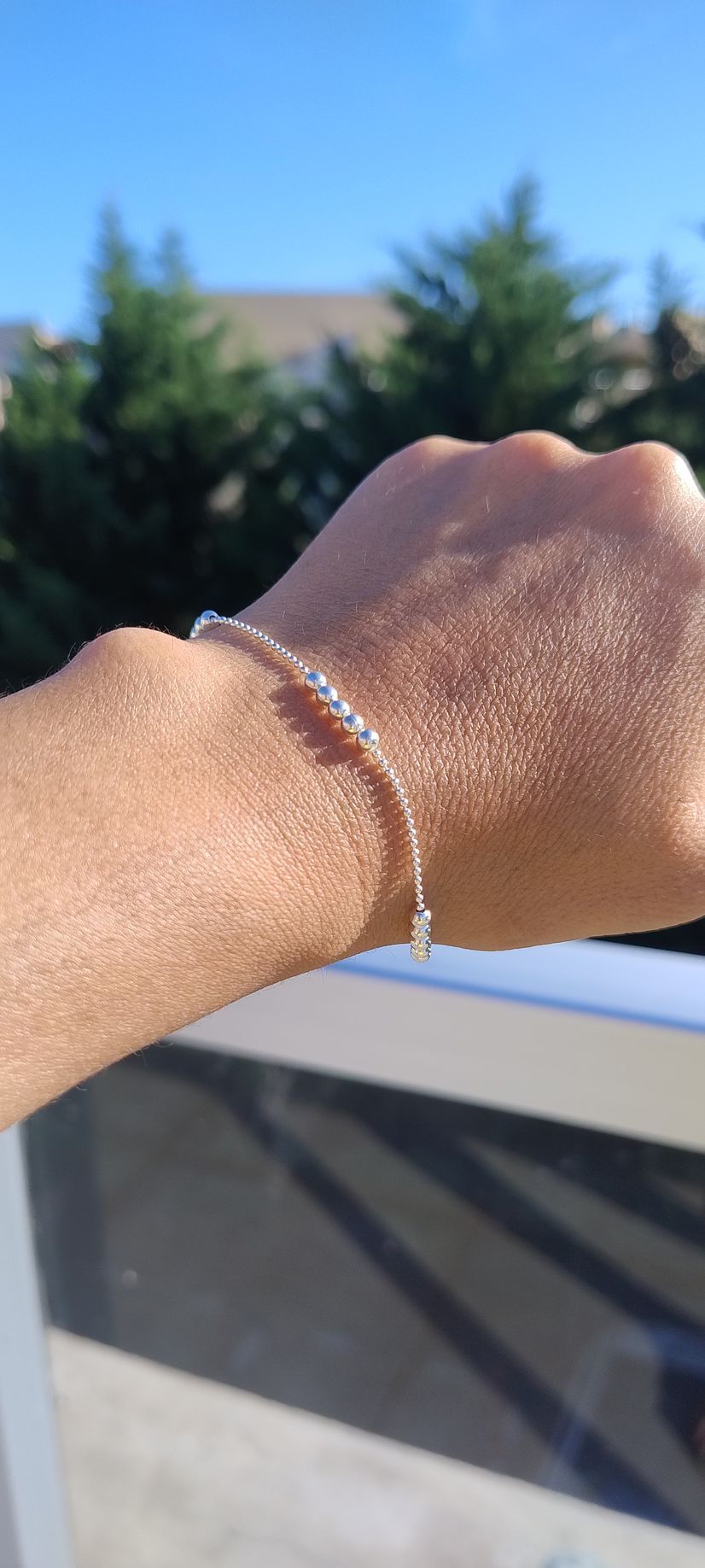 Muñeca con pulsera alzada contra un soleado paisaje exterior con árboles y cielo azul.