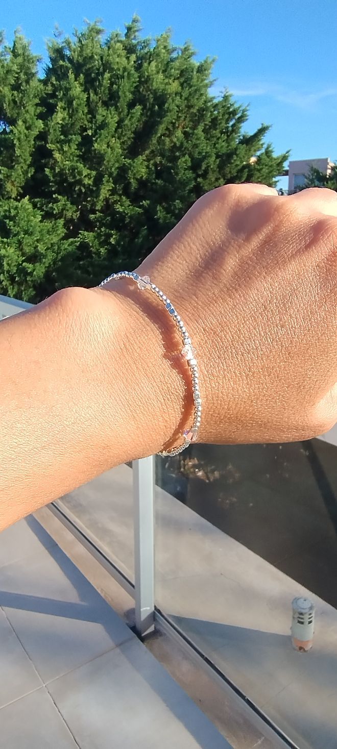 Primer plano de una muñeca con una pulsera de plata sobre un fondo soleado al aire libre.