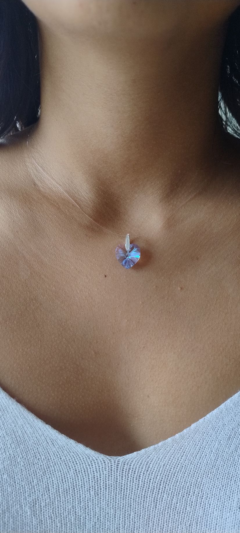 Primer plano de un collar con un pequeño colgante azul y rosa en una persona que lleva una blusa blanca.