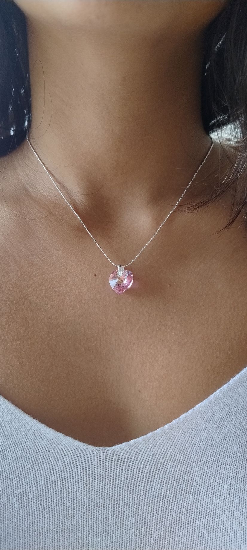 Primer plano de un collar de plata con un colgante rosa sobre una blusa de punto blanca.