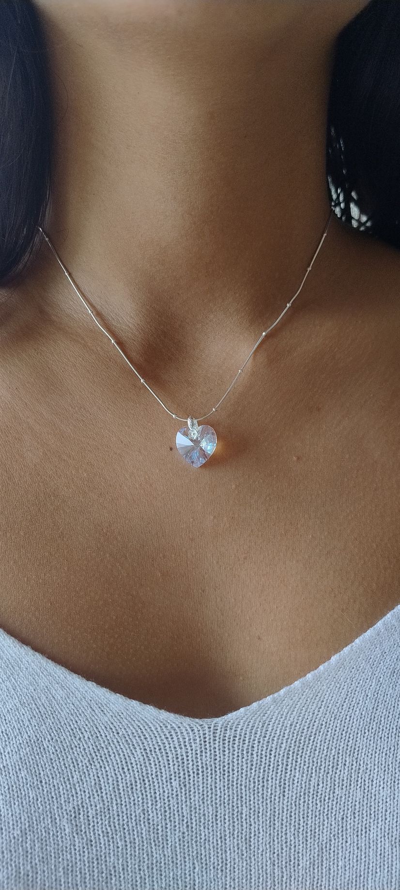 Primer plano de una persona que lleva un collar de plata con un colgante en forma de corazón y una blusa blanca.