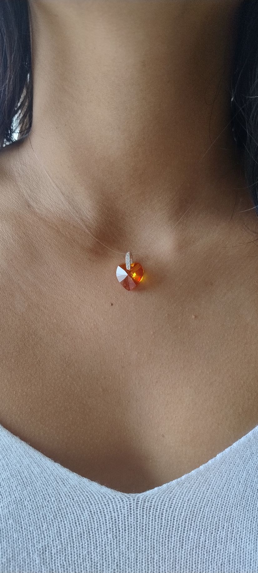 Primer plano del cuello y el pecho de una persona que luce un pequeño colgante de piedra preciosa naranja en una cadena fina.
