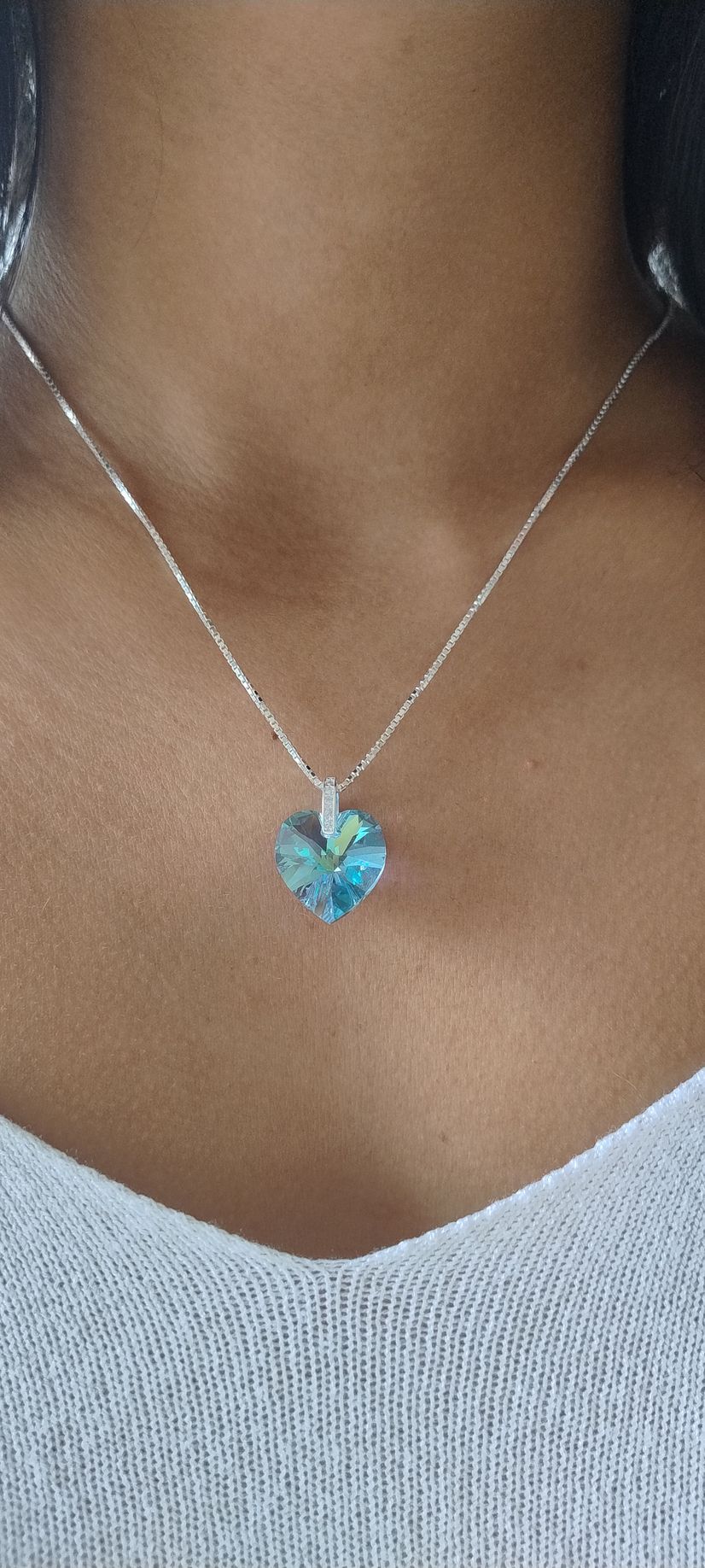 Primer plano de un collar de plata con un colgante de corazón azul sobre una base blanca.