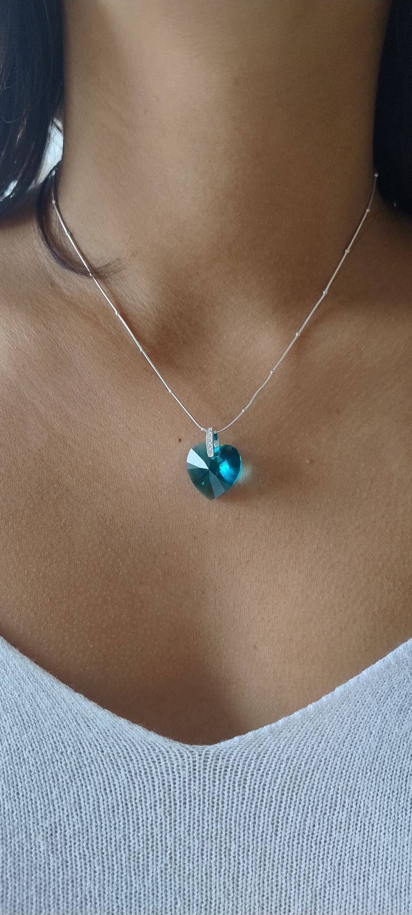 Primer plano de un collar de plata con un colgante de turquesa sobre una blusa blanca con escote en V.