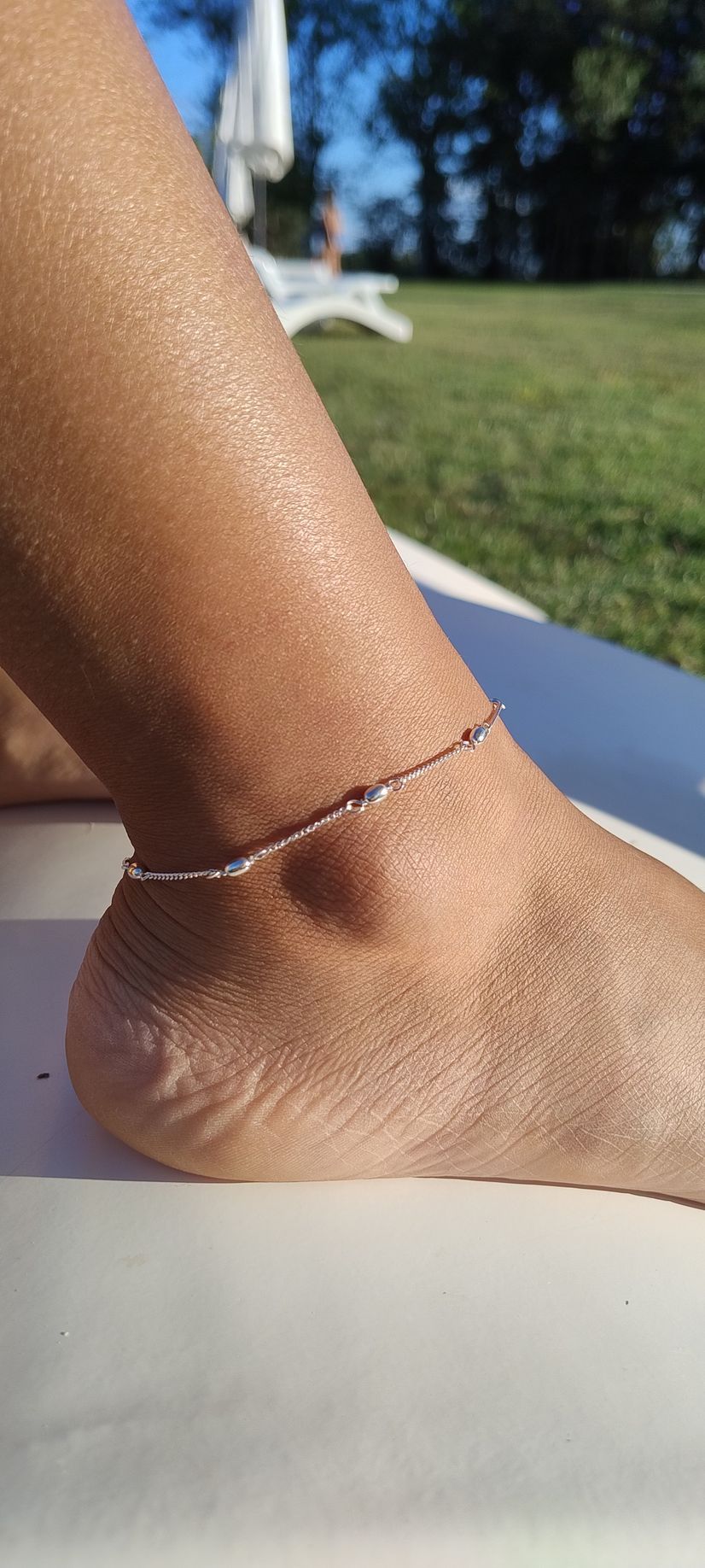 Primer plano de un tobillo con una delicada pulsera de cuentas bajo la luz del sol, con la hierba
