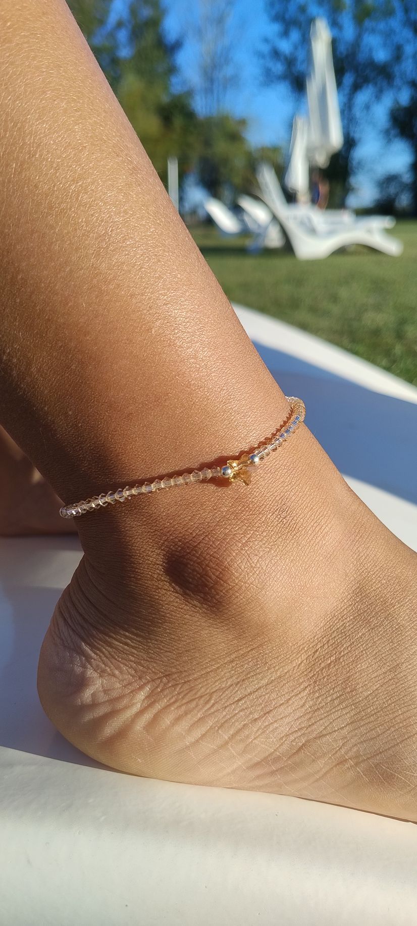Primer plano de un tobillo con una delicada pulsera de cuentas, al aire libre en un día soleado.