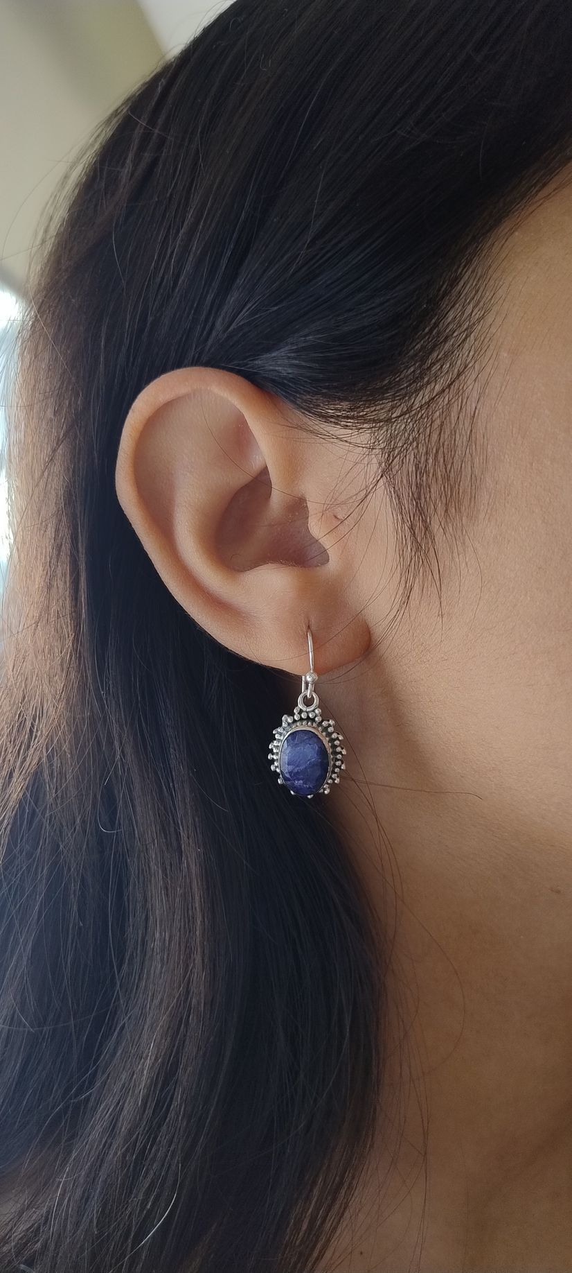 Primer plano de la oreja de una persona que lleva un pendiente colgante azul y plateado.