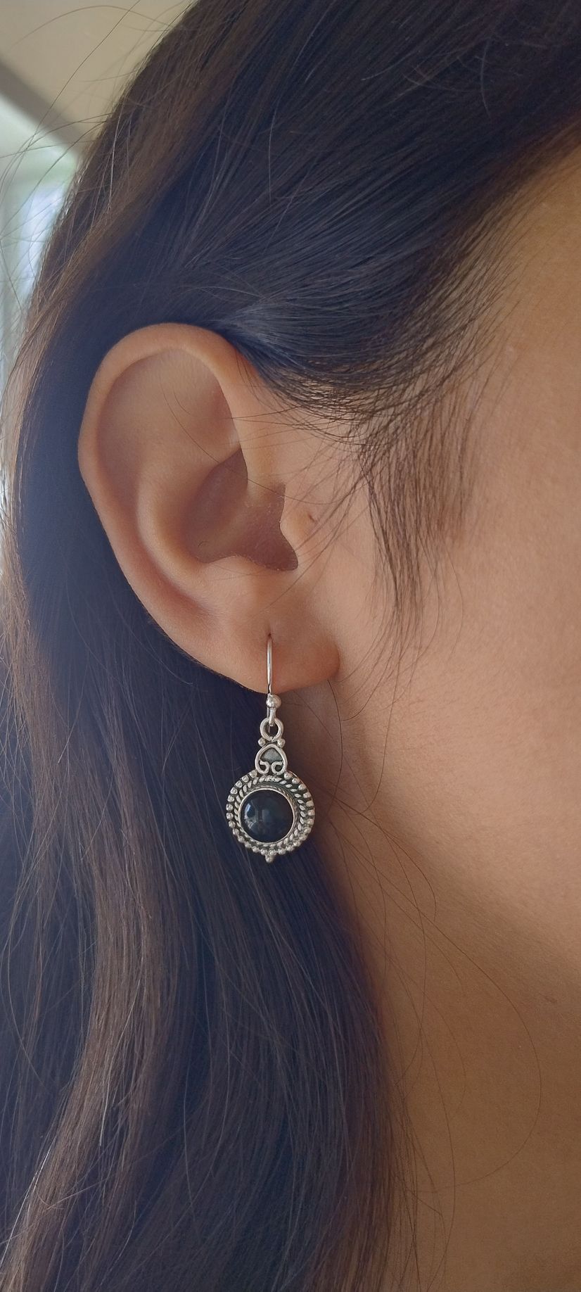 Primer plano de una oreja con un pendiente de plata en forma de lágrima y cabello oscuro sobre un fondo desenfocado.