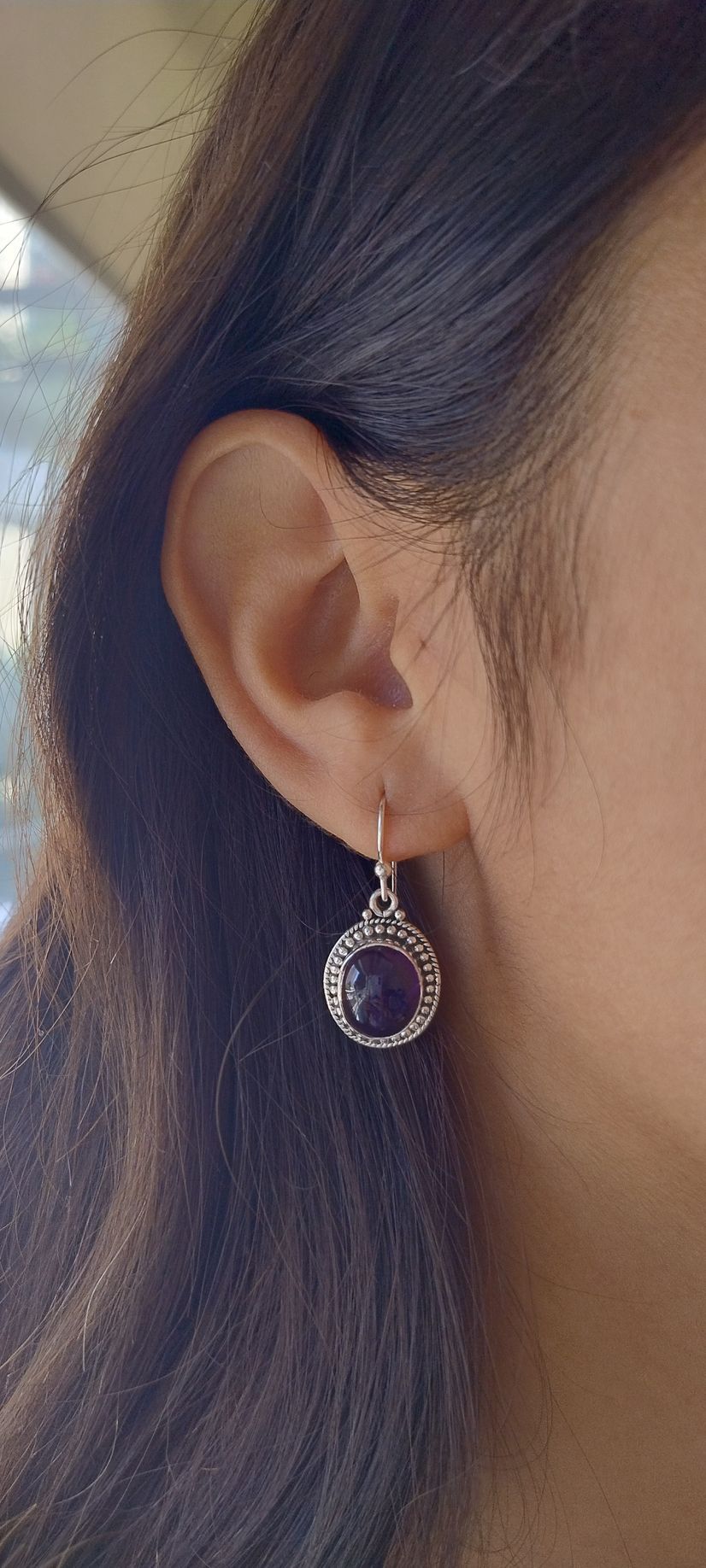 Primer plano de la oreja de una mujer con un pendiente colgante en forma de lágrima y un aro en la nariz.