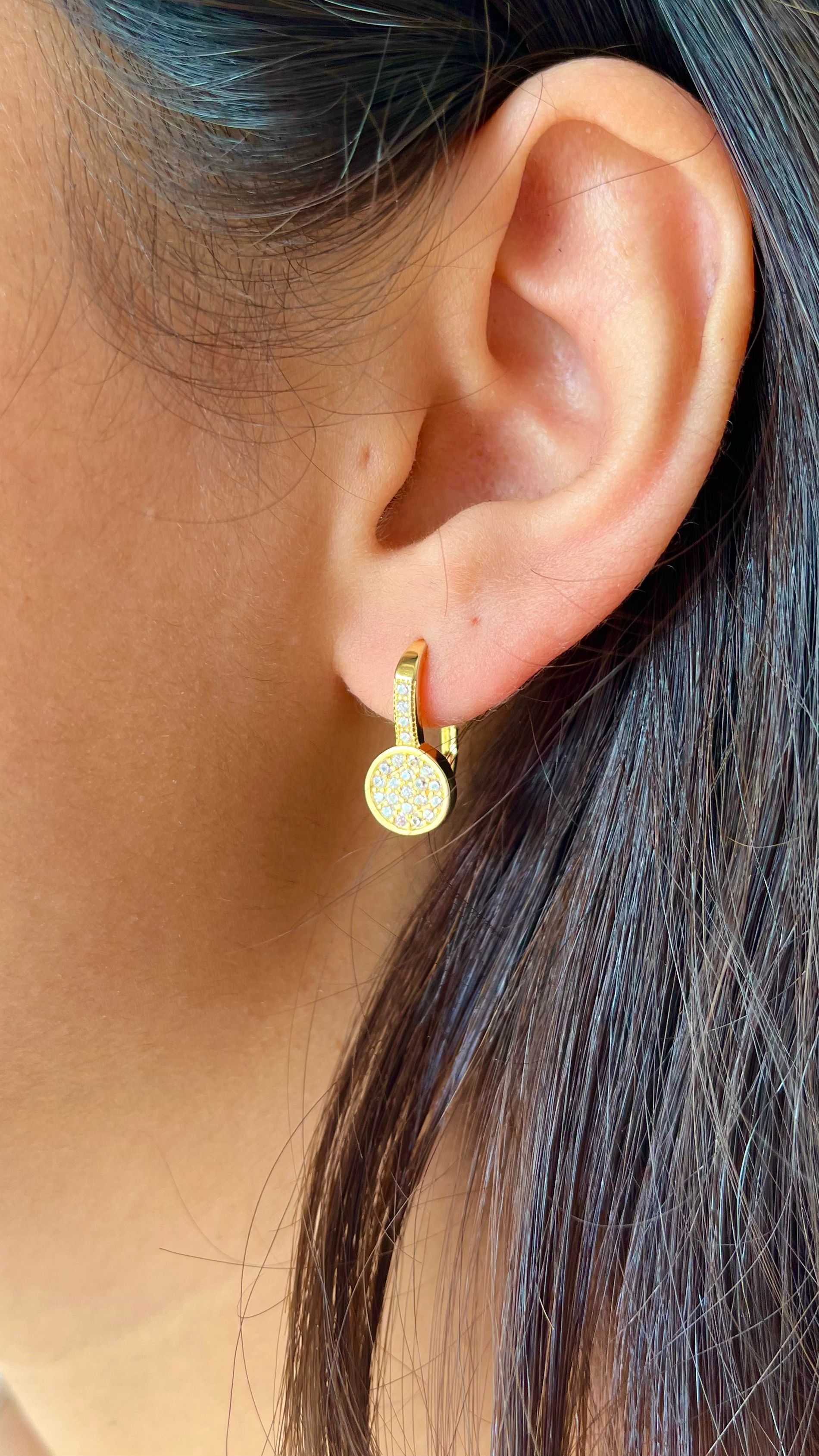 Primer plano de una oreja con un pequeño aro de oro y un pendiente colgante redondo.
