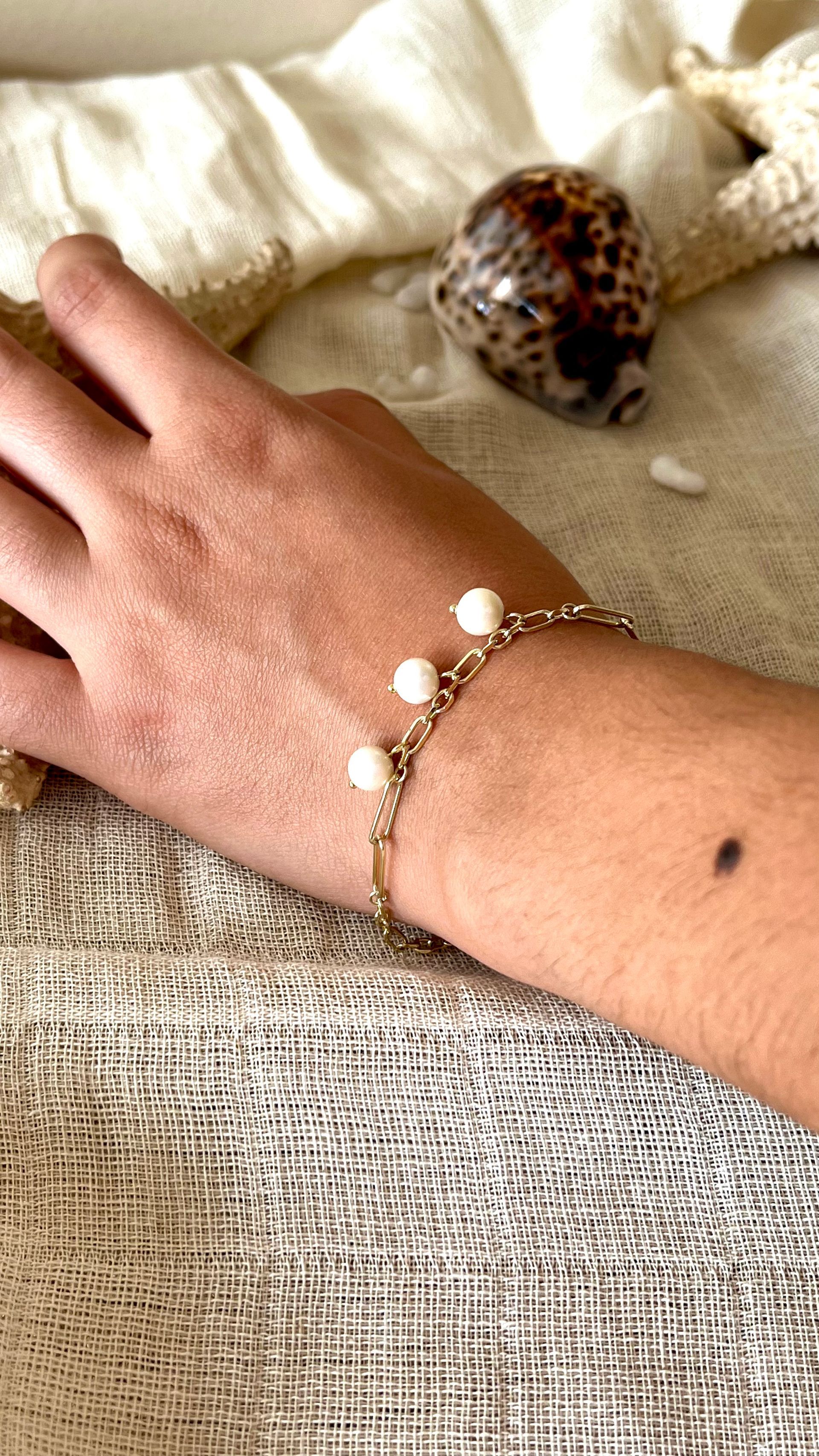 Primer plano de brazos cruzados con una pulsera de cuentas doradas y una blusa blanca sin mangas.