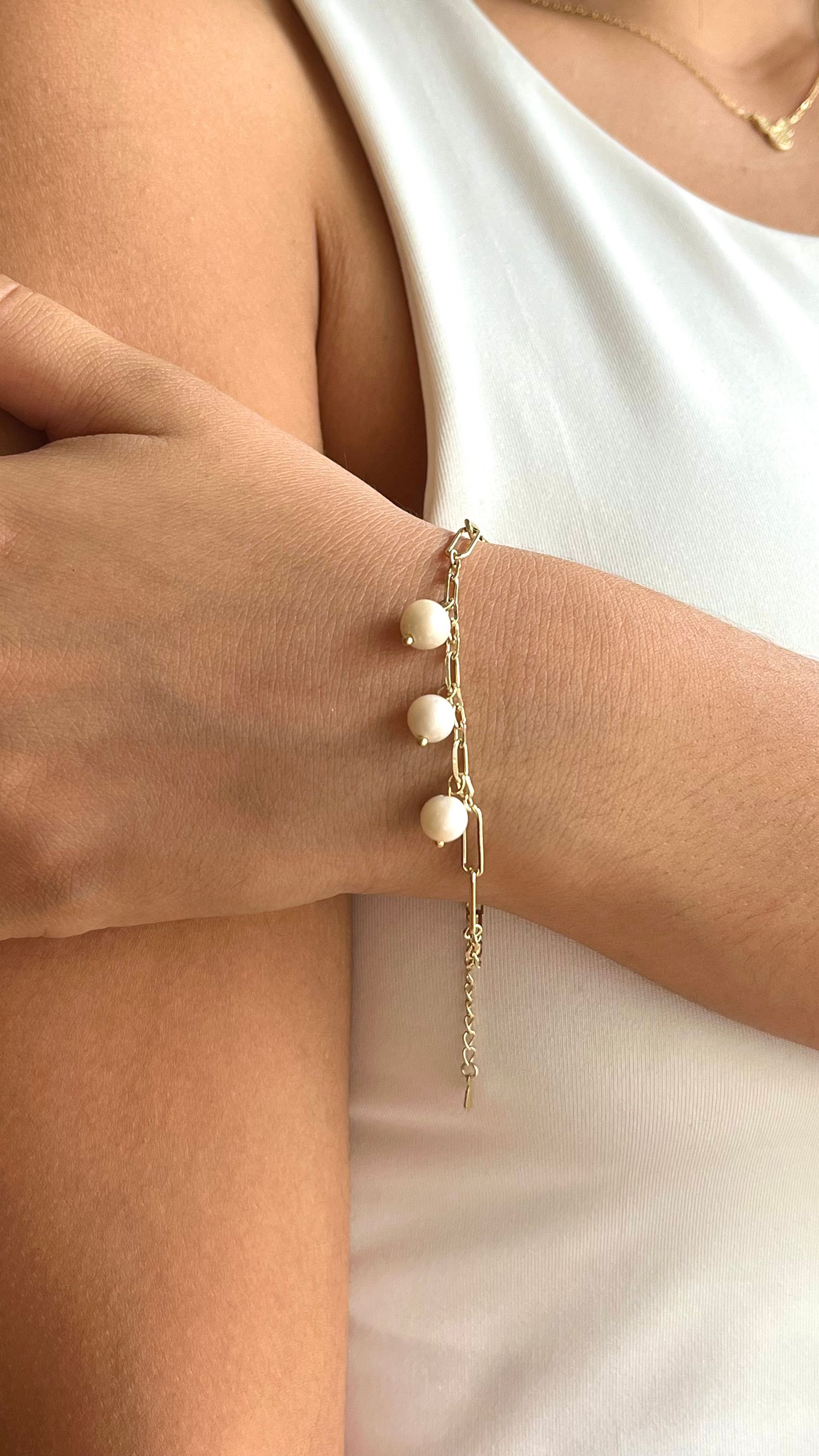 Primer plano de brazos cruzados con una pulsera de cuentas doradas y una blusa blanca sin mangas.