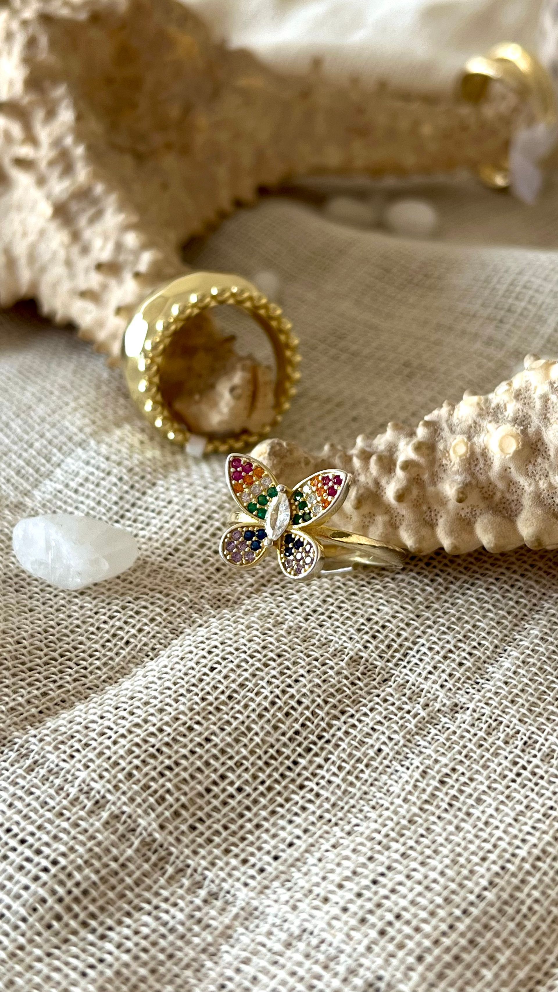 Primer plano de una mano con un anillo de piedras preciosas de colores que descansa sobre un brazo vestido de blanco.