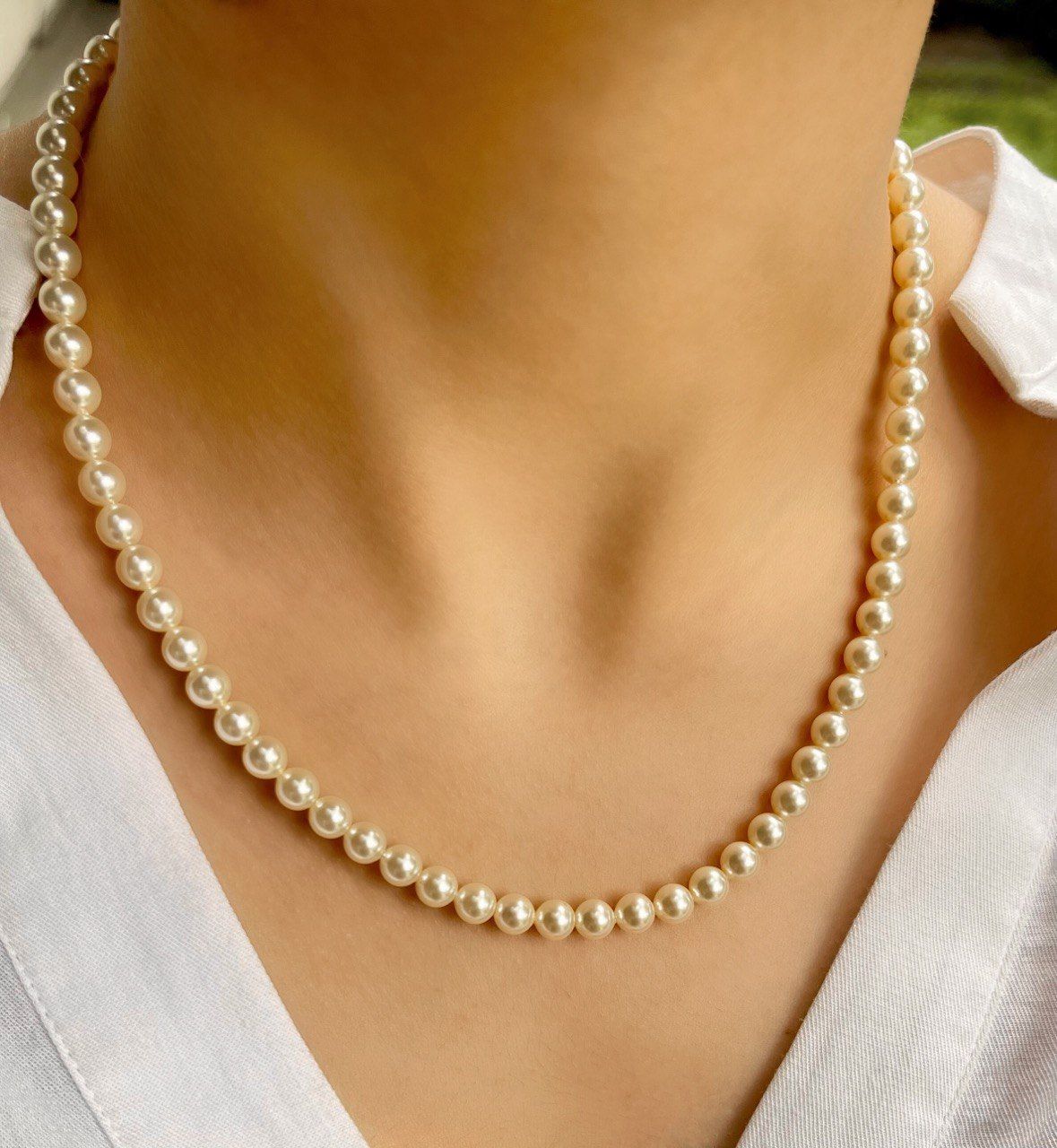 Mujer que lleva un collar de perlas color crema; se aprecia el escote y la camisa blanca.