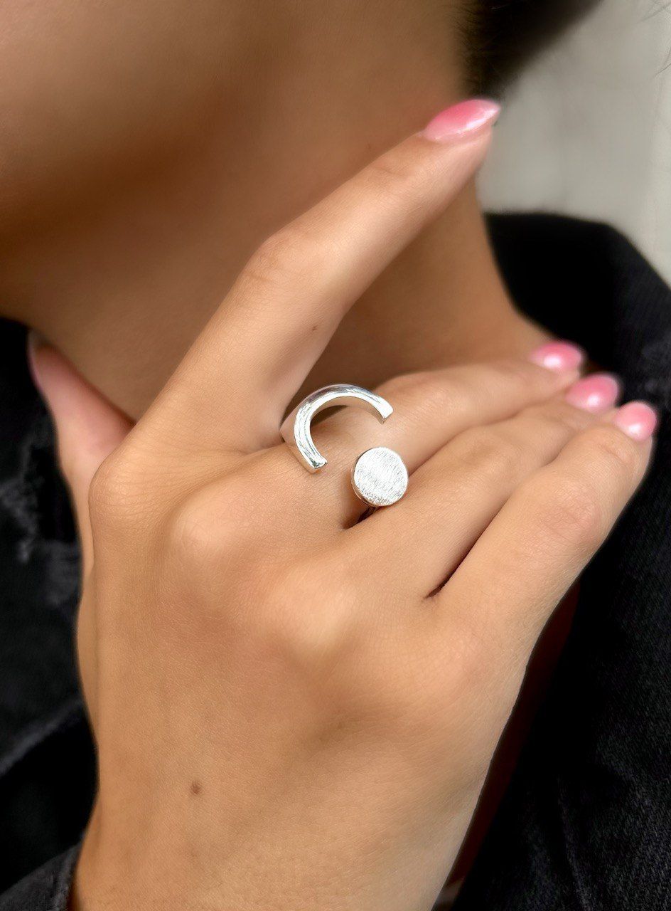 Una mano que luce un anillo de plata con una banda curva y una piedra redonda y blanca.