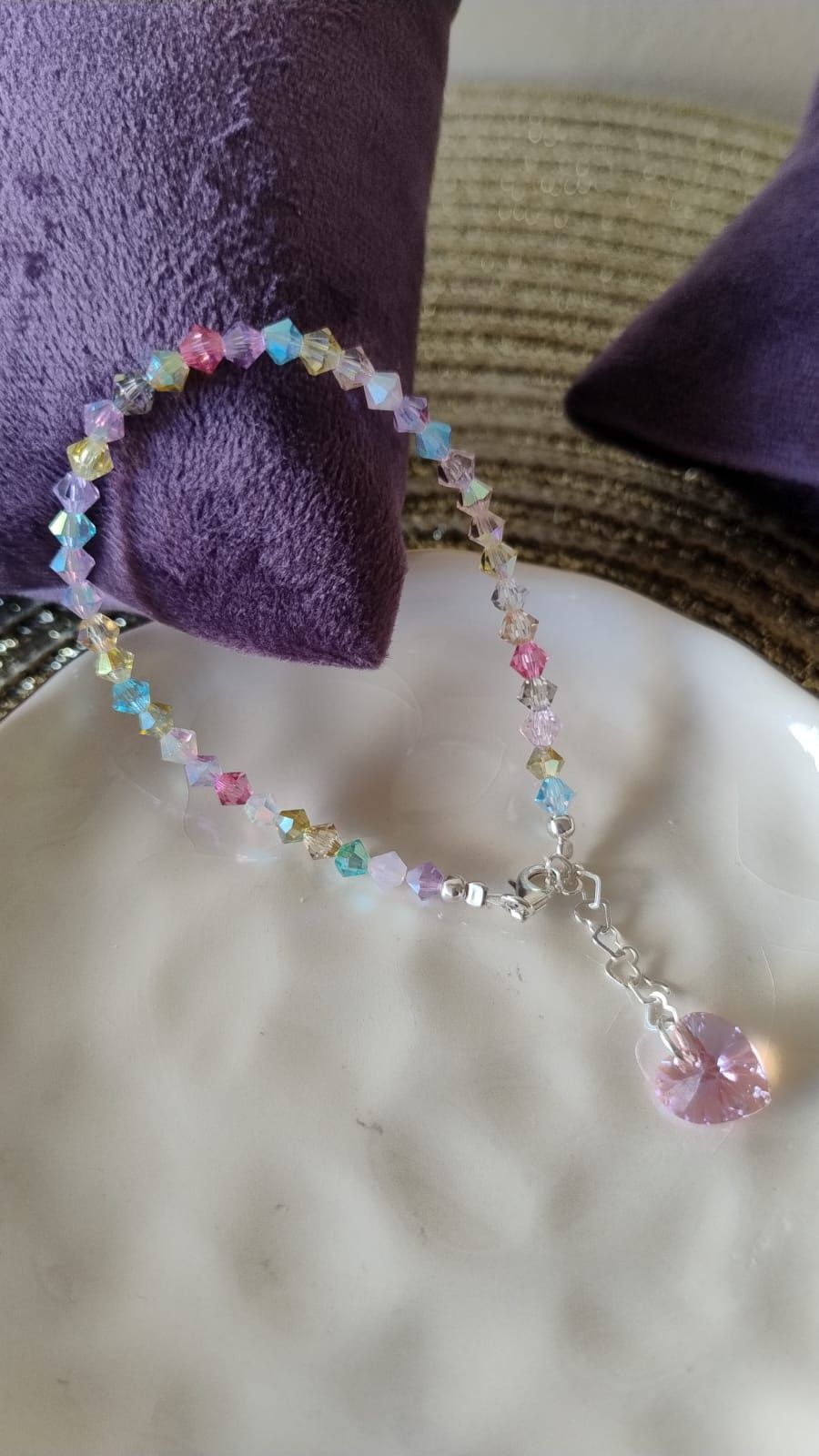 Pulsera con cuentas de colores y un dije de cristal rosa, sobre un plato blanco.