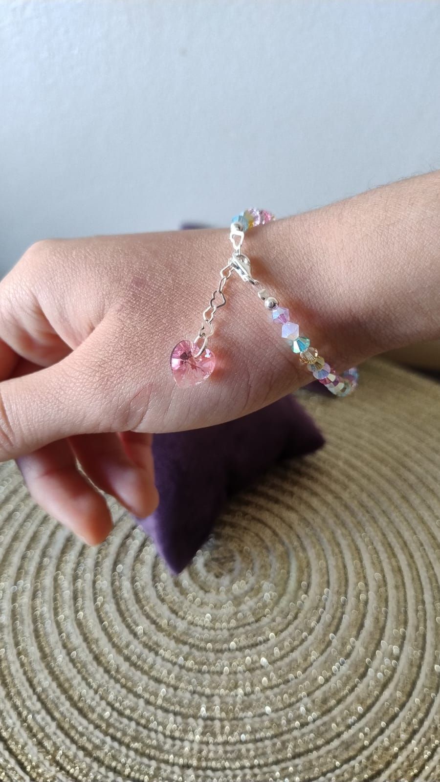 Pulsera con cuentas de colores y un dije de cristal rosa, sobre un plato blanco.