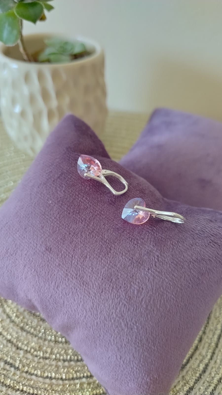 Dos pendientes de plata con cuentas de cristal rosa sobre un cojín de terciopelo morado.