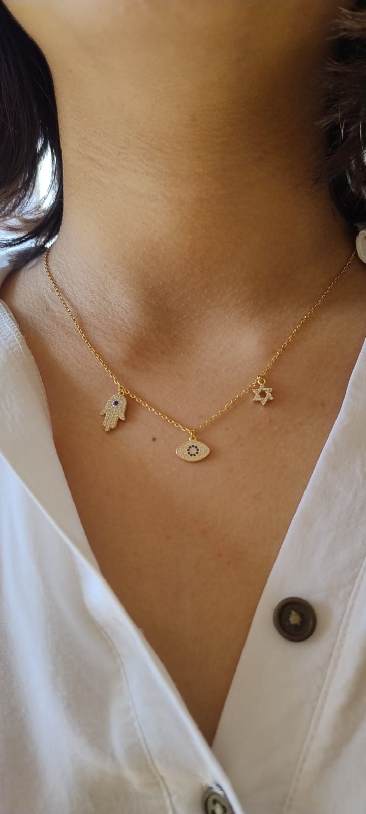 Primer plano de un collar de oro en capas con un colgante de flor sobre el escote de una blusa blanca.