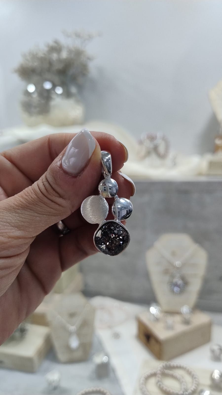 Mano sosteniendo un colgante de cuentas de plata en una vitrina de joyería.