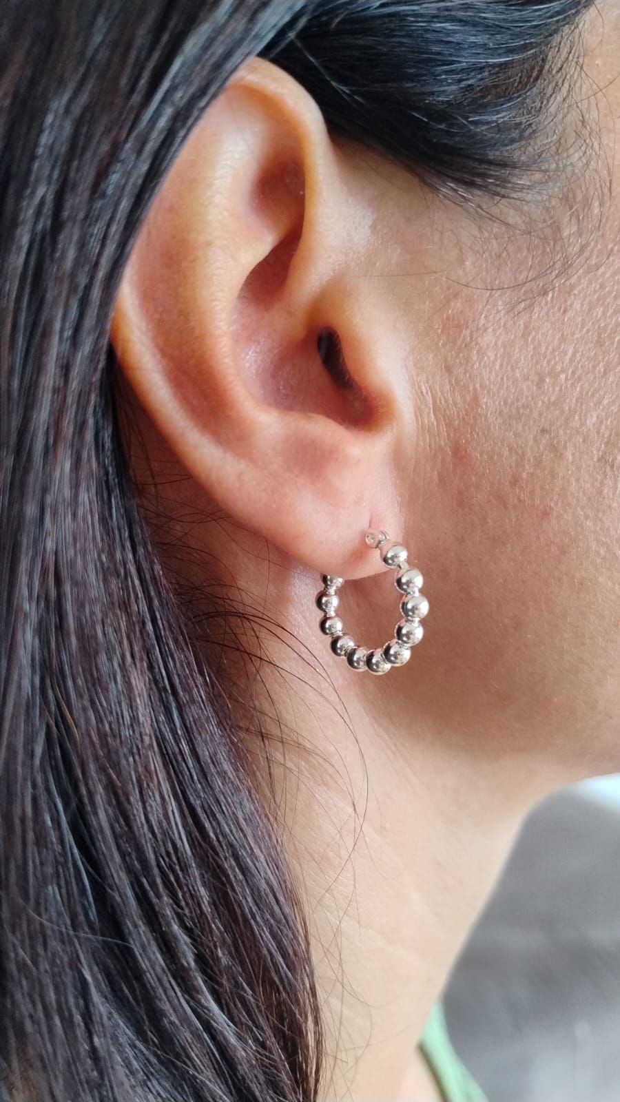 Primer plano de una oreja con un pendiente de aro plateado y cabello largo y oscuro.