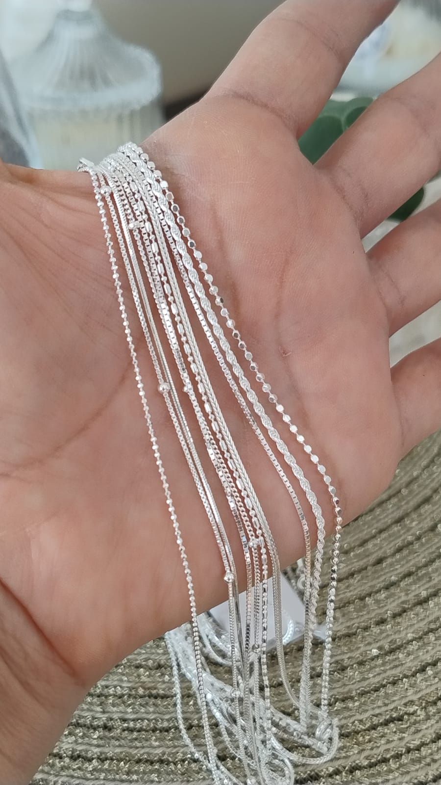 Mano sosteniendo varios delicados collares de cadena de plata con pequeños colgantes.
