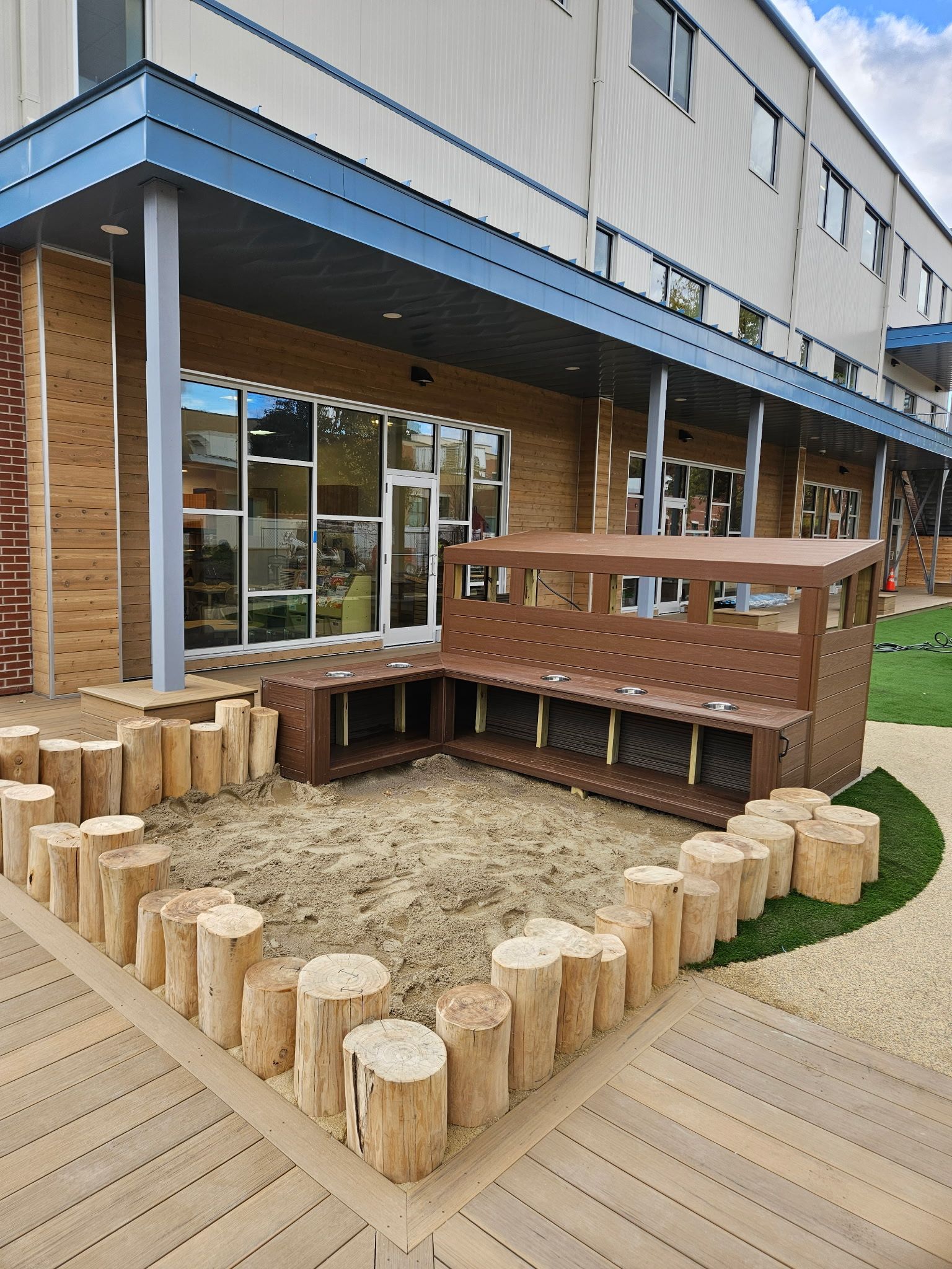 Outdoor sandbox area with log border and wooden play structure near a building.