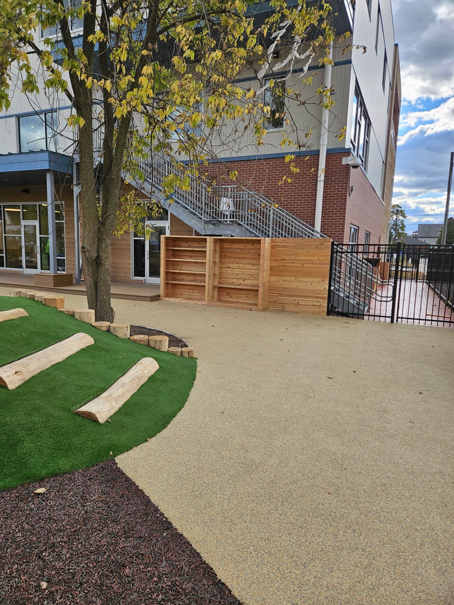 Exterior view of building with pathway, wooden fence, grass, tree and decorative pavers.