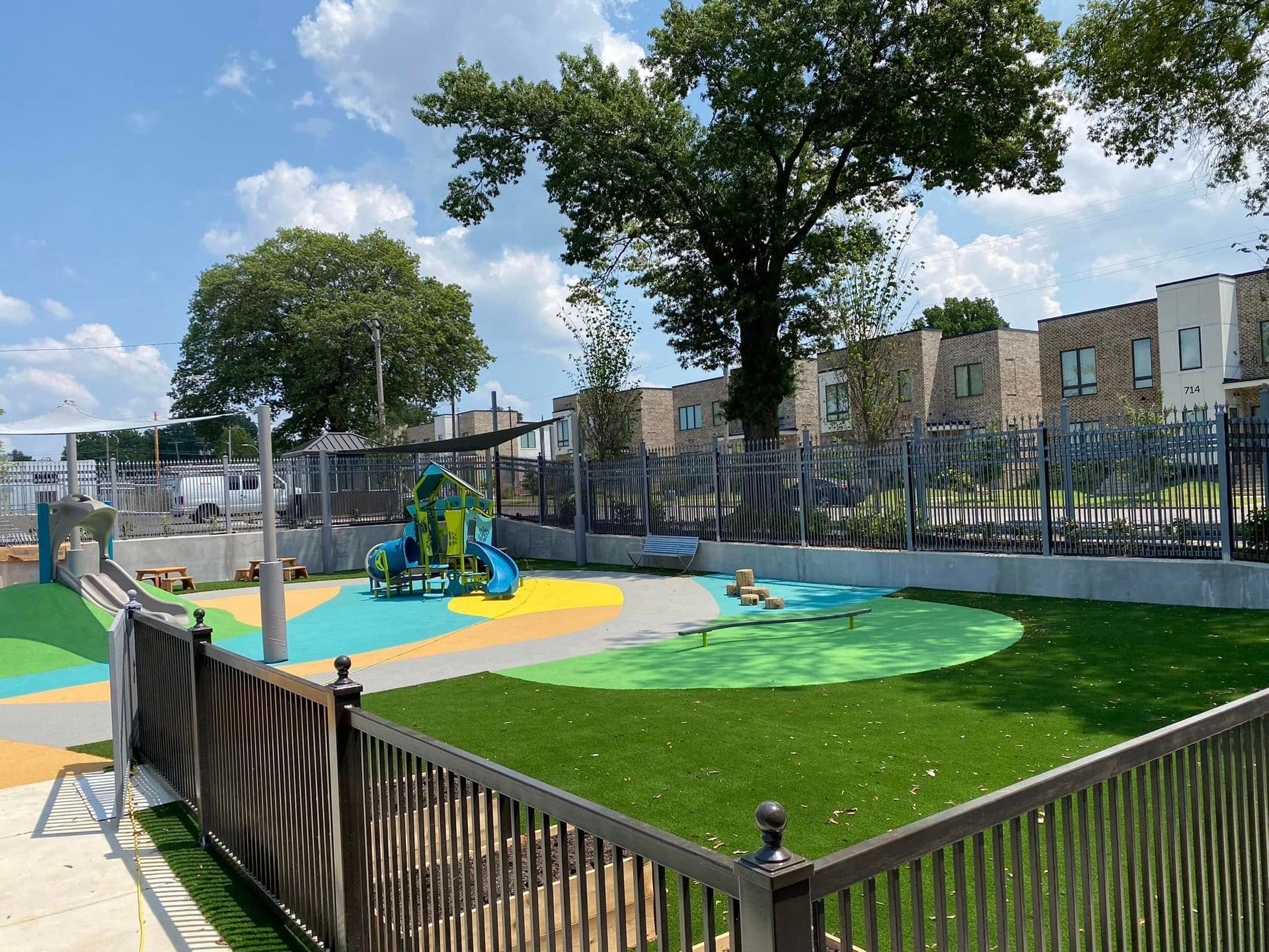 Playground with colorful play equipment, artificial turf, and a fence, sunny day.