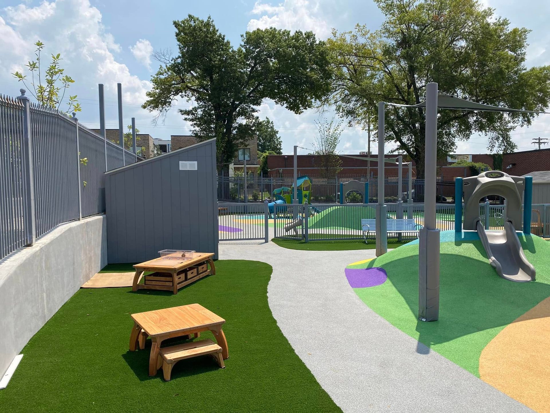 Playground with artificial turf, picnic tables, a slide, and a gray fence.