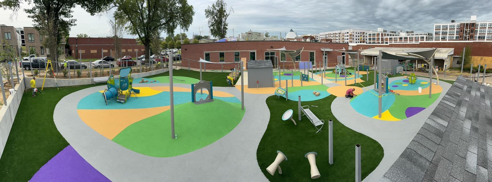 A colorful, modern playground with various play structures and patterned flooring, set outdoors.
