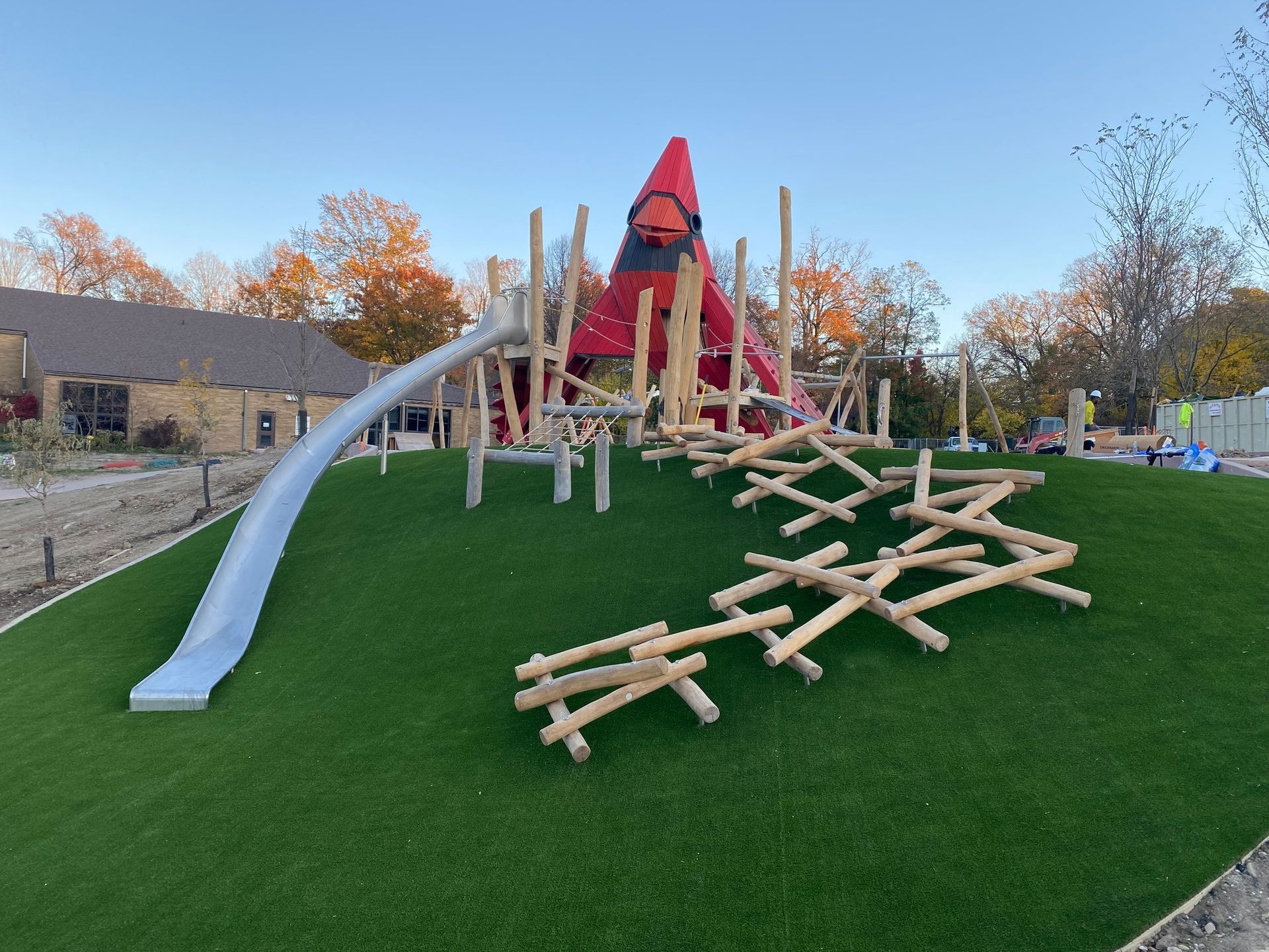 Playground with slide, climbing structures, and red accent piece, set on artificial green grass.