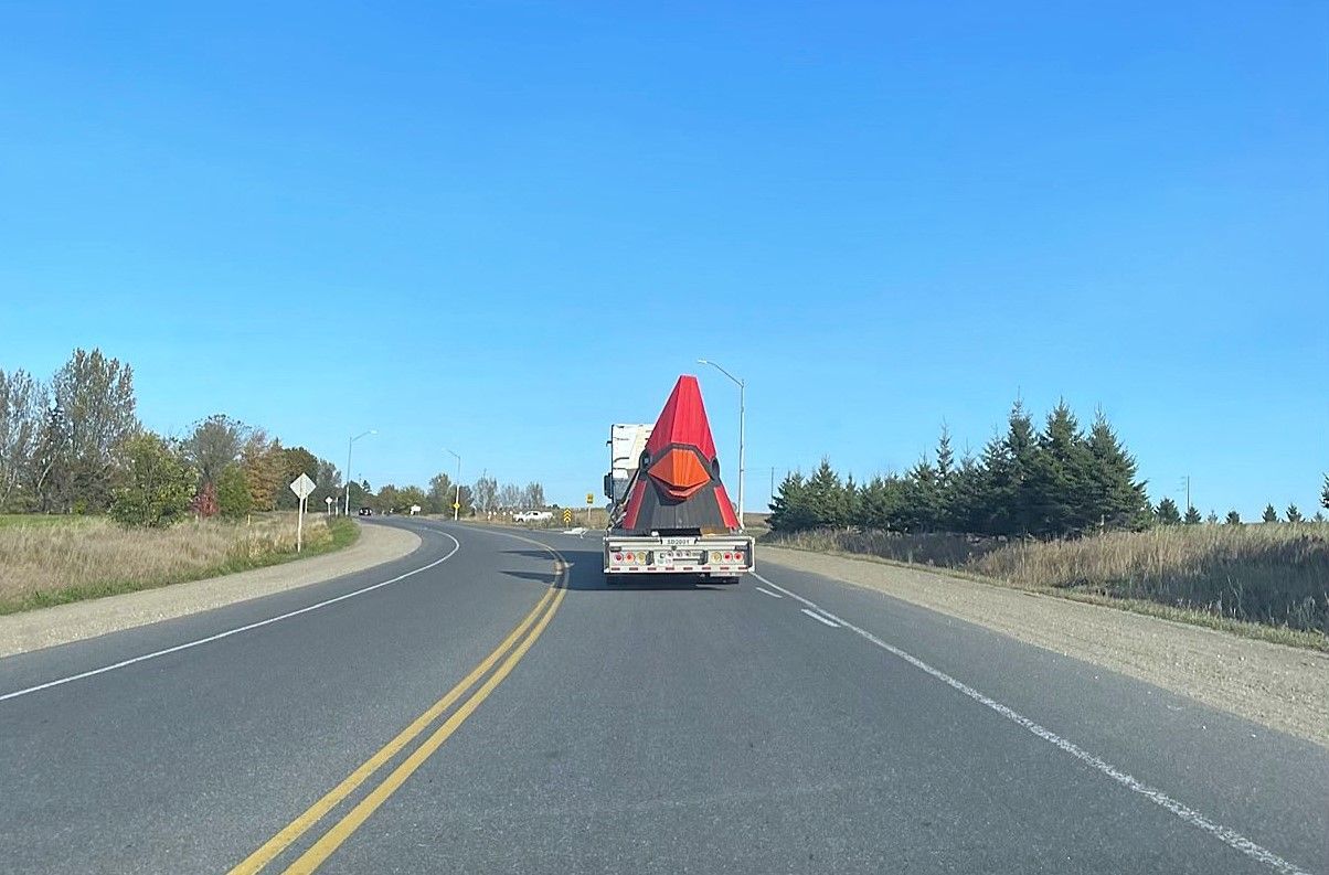 A large red and white truck drives along a curving asphalt road under a clear blue sky.