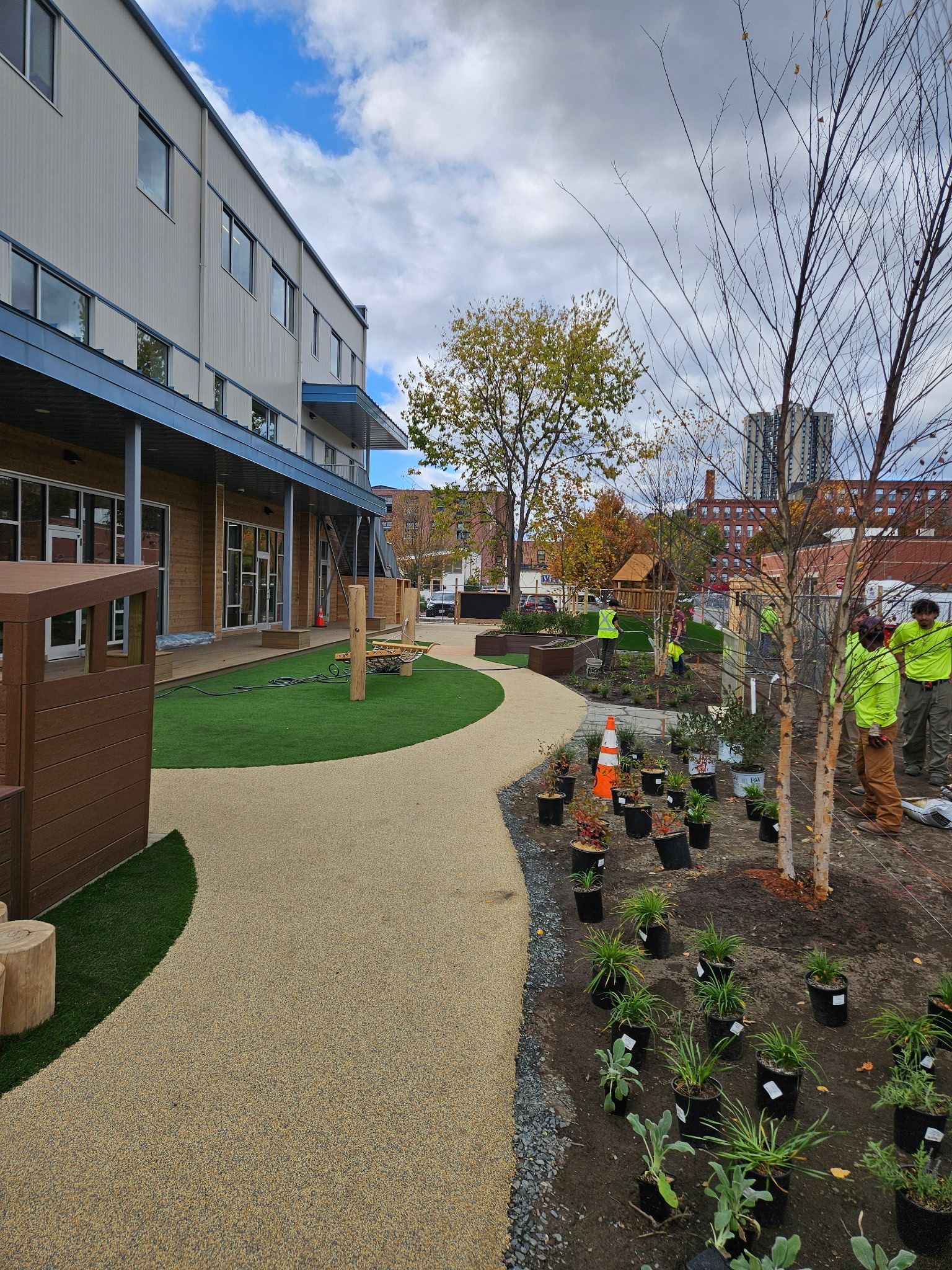 Exterior of a building with a playground and landscaped garden. Workers in safety vests are present.