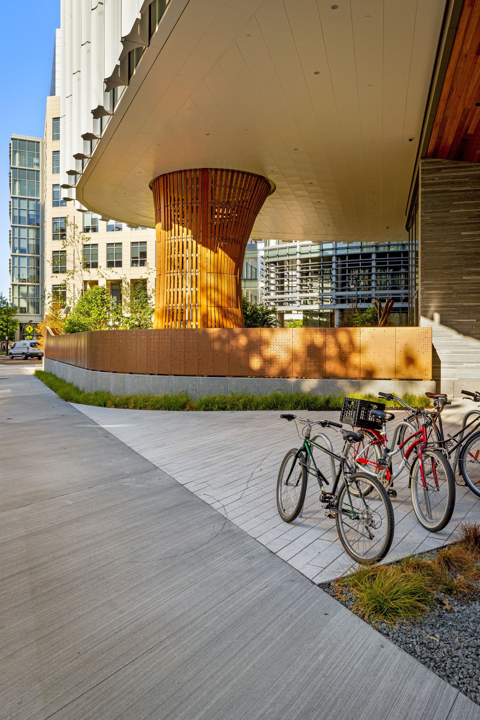 Bicycles parked on a sidewalk under a building overhang. A wooden pillar supports the overhang.