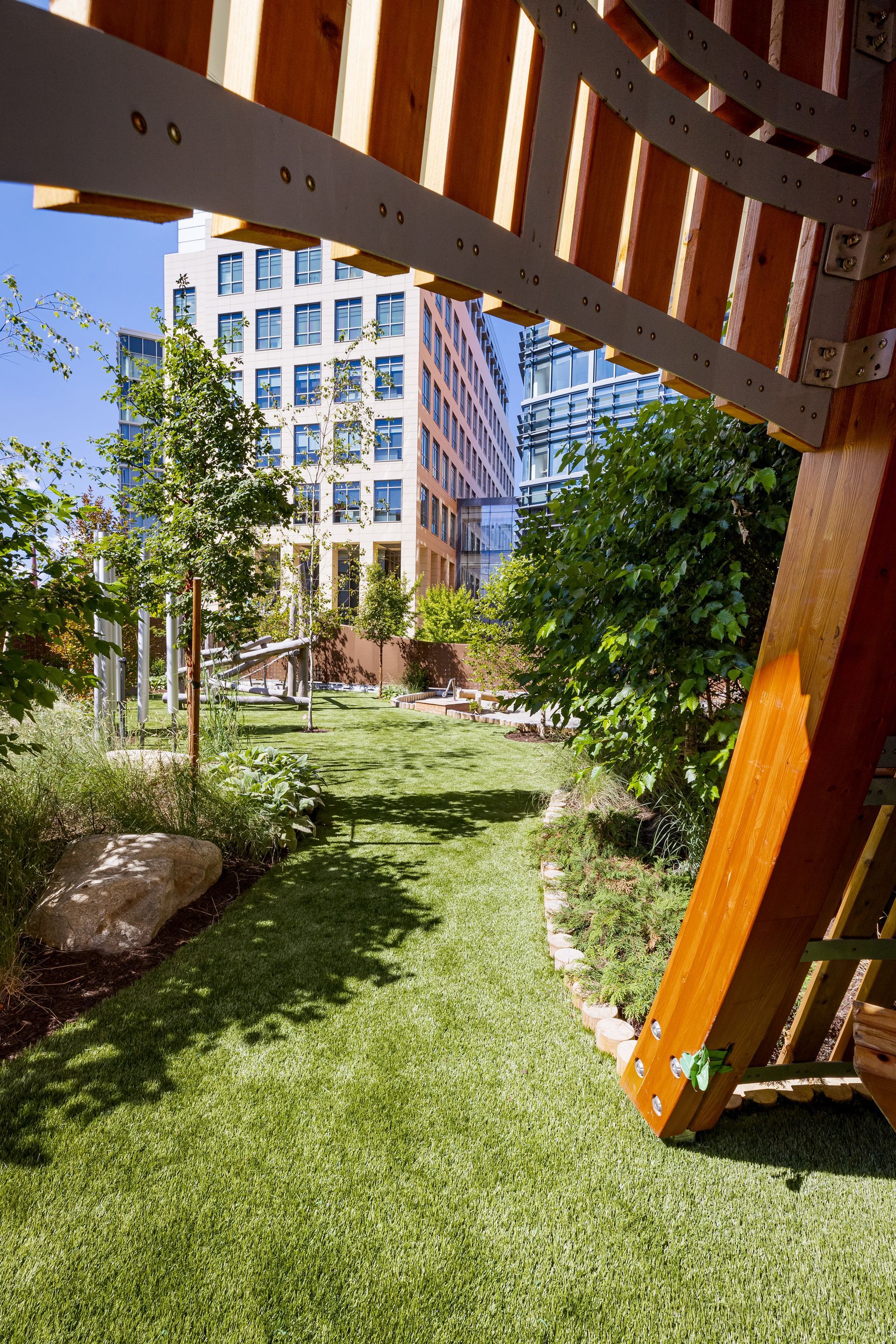 Looking out from a wooden structure to a green lawn in a city park, with buildings in the background.