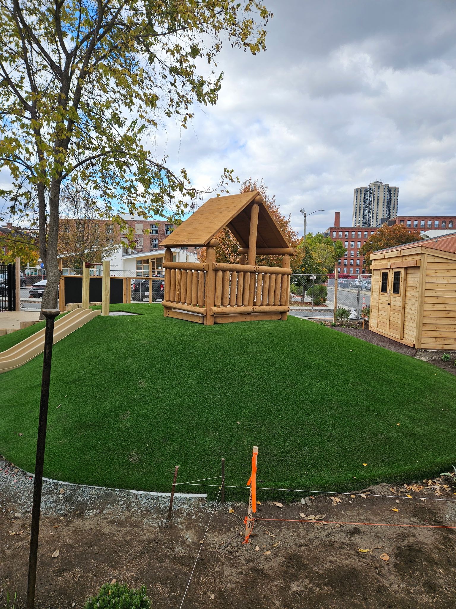 Playground with wooden structures on a grassy hill, against a cloudy sky.