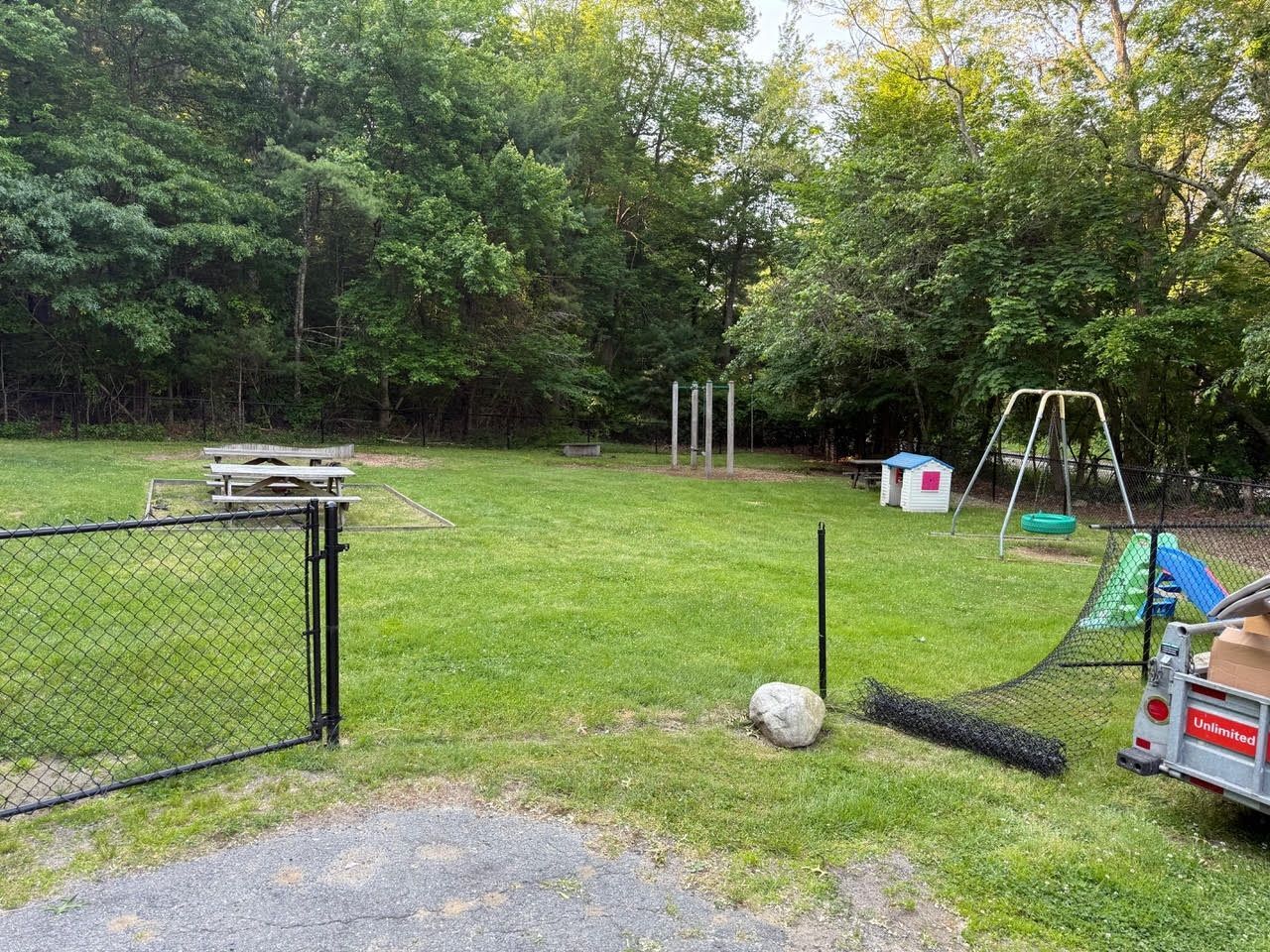 A fenced backyard with grass, a playground, picnic table, and trees.