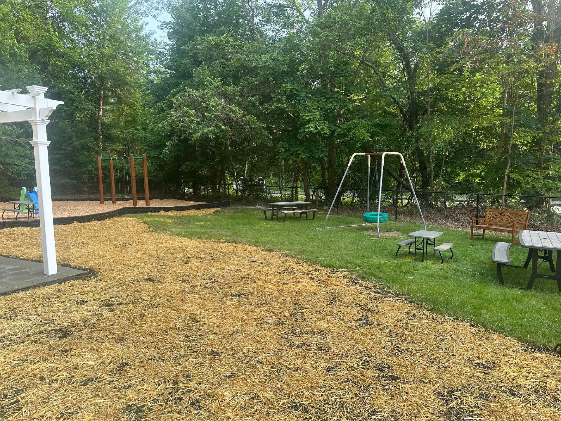 Playground with mulch, swings, picnic tables, and trees in background.