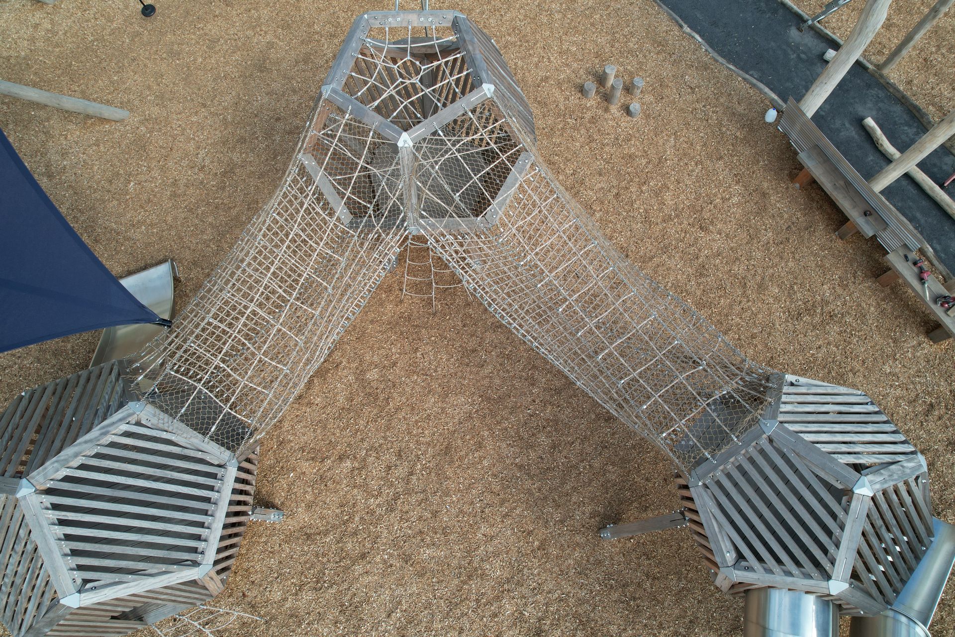 Overhead view of a wooden playground structure with rope climbing tunnels, a boat, and wood-chip ground covering.