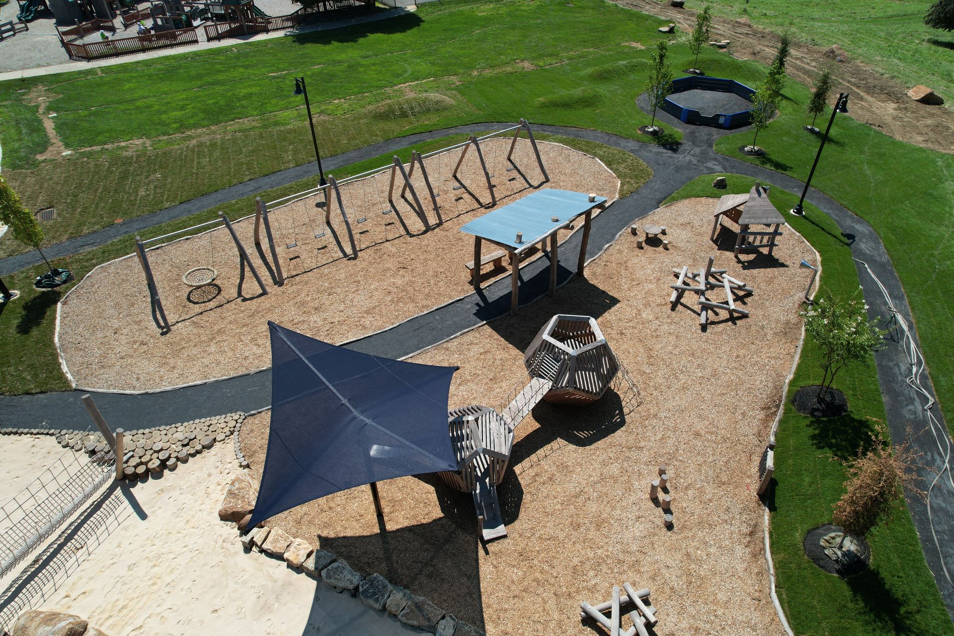 Aerial view of a playground with swings, climbing structures, a shelter, and wood chip ground cover.