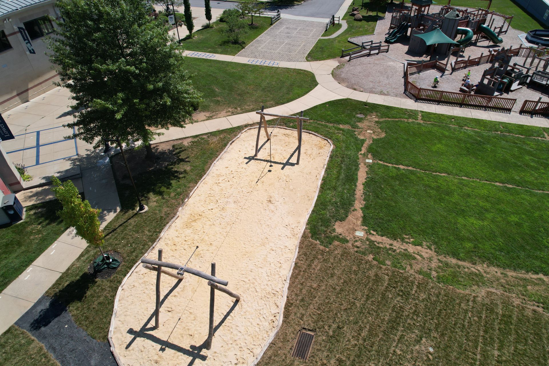 Overhead view of a playground with sand pit and wooden climbing structures surrounded by grass and walkways.