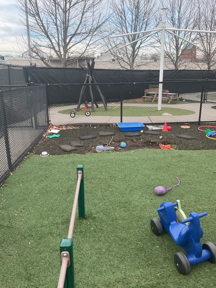 Playground with green turf, equipment, and toys behind a black fence.