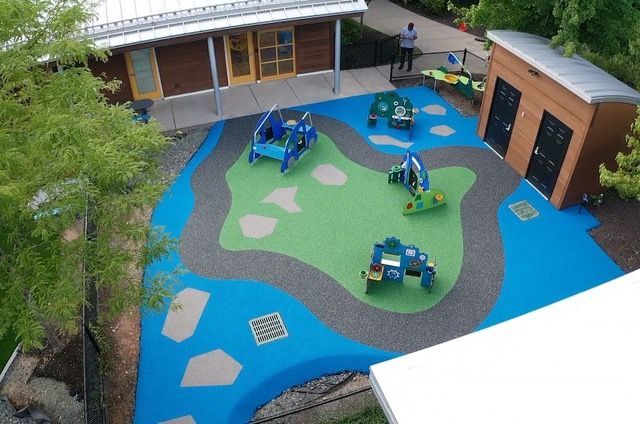 Playground with blue and green rubber surfacing, toy cars, and a small building.