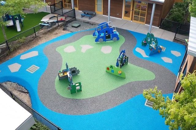 Playground with blue, green, and gray rubber surfacing. Play equipment includes trucks and climbing structures.