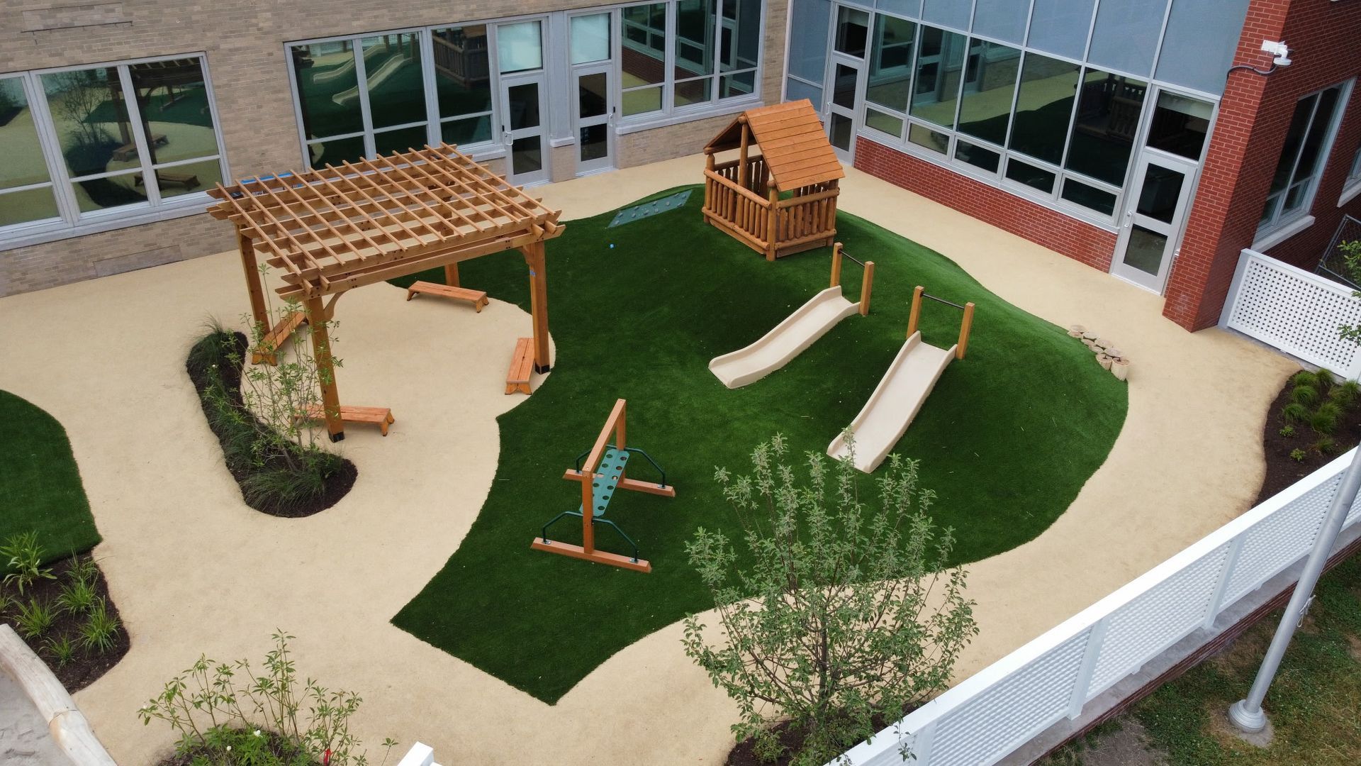 A playground area with a green shade canopy, picnic benches, and trees, enclosed by a black chain-link fence.